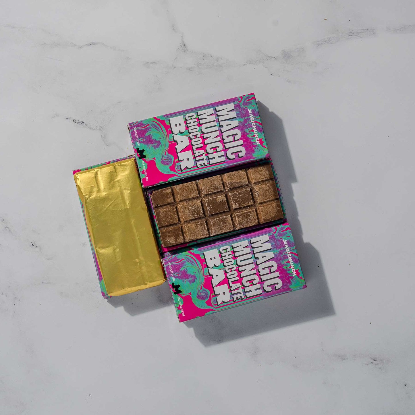 Magic Munch Chocolate Bar laying down in between six Magic Munch Chocolate Bar Boxes and one choclate bar wrapped in a gold paper